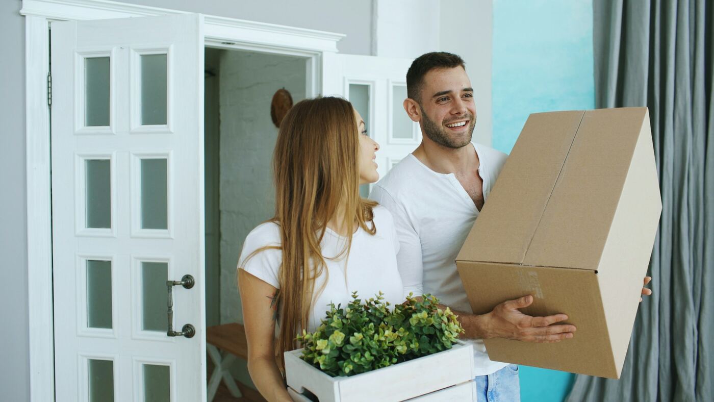 Zwei Personen tragen Umzugskartons in eine helle Wohnung